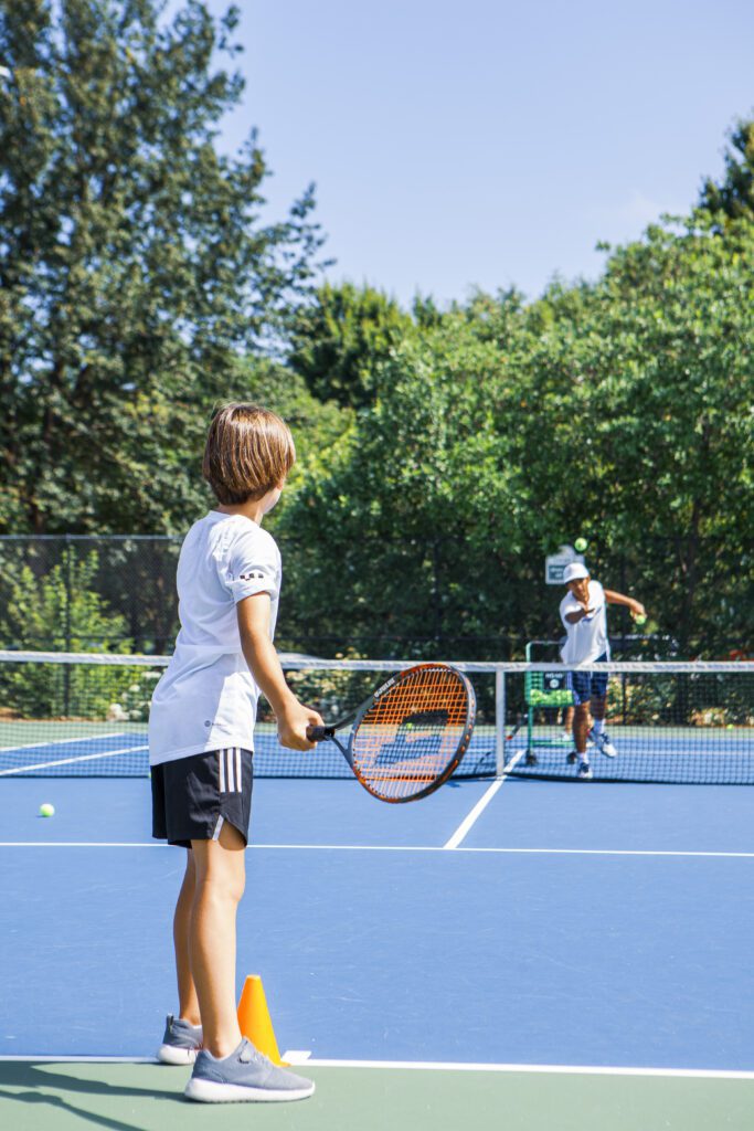 A young boy stands at the edge of a tennis court waiting to serve with a racket in his hand during the St. Louis Tennis Club's summer camp. 