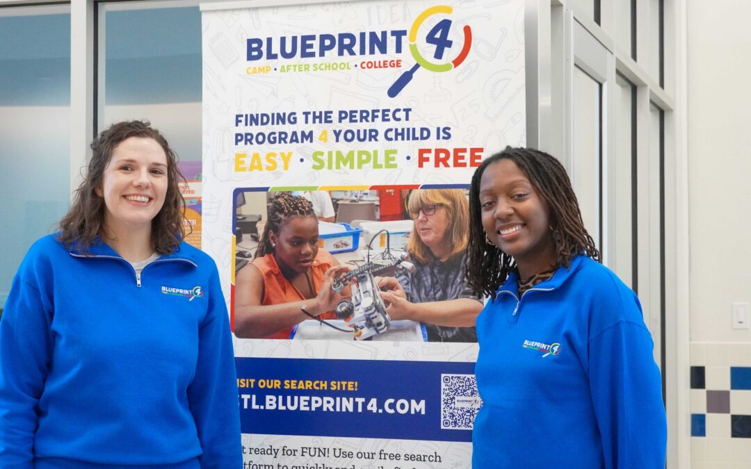 Blueprint4 staff members, Abbey and Sarah, stand on either side of a tall banner with the Blueprint4 logo and a photo of a girl at a summer robotics camp