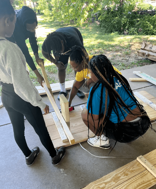 A group of teens work together to build a wooden bench at the Gateway Region YMCA summer camp.