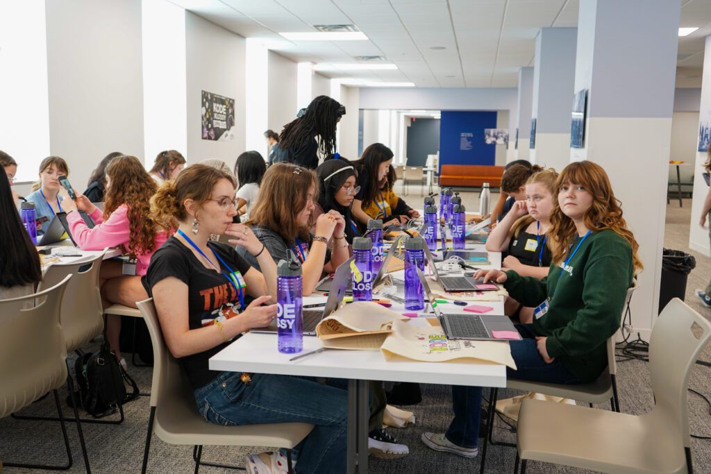 A long table of young women work on laptops at the Kode with Klossy summer camp.