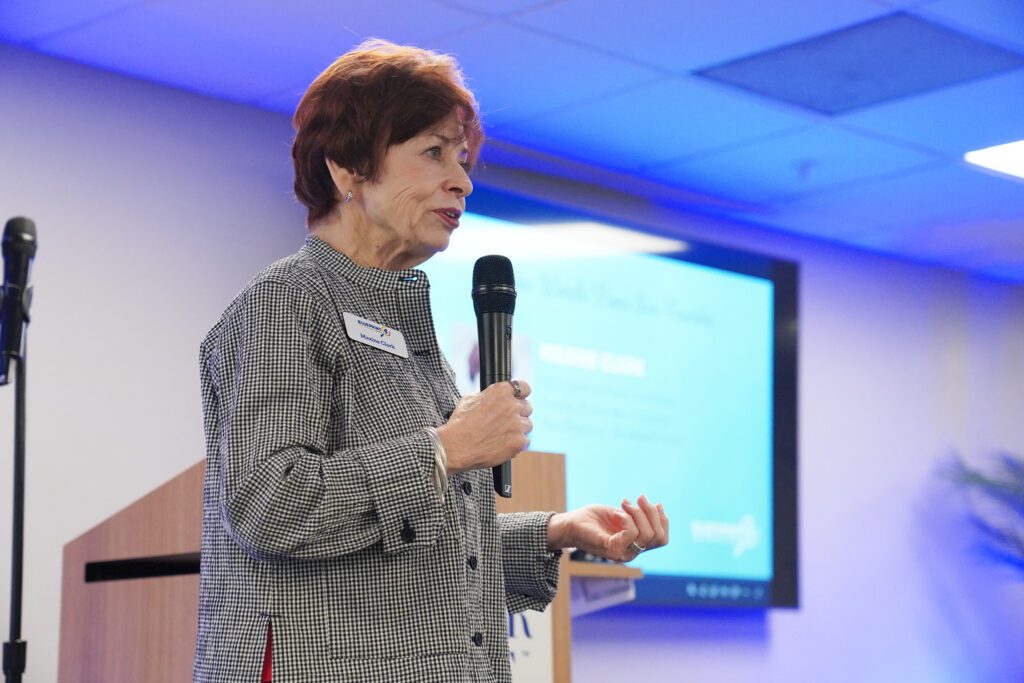 blueprint4 founder Maxine clark gives a speech on stage. She stands in front of the podium and the wall behind her is lit up blue. 