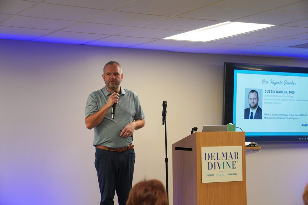 Dustin Nadler holds a microphone while speaking to the crowd. He talks through the survey results from St. Louis families. 