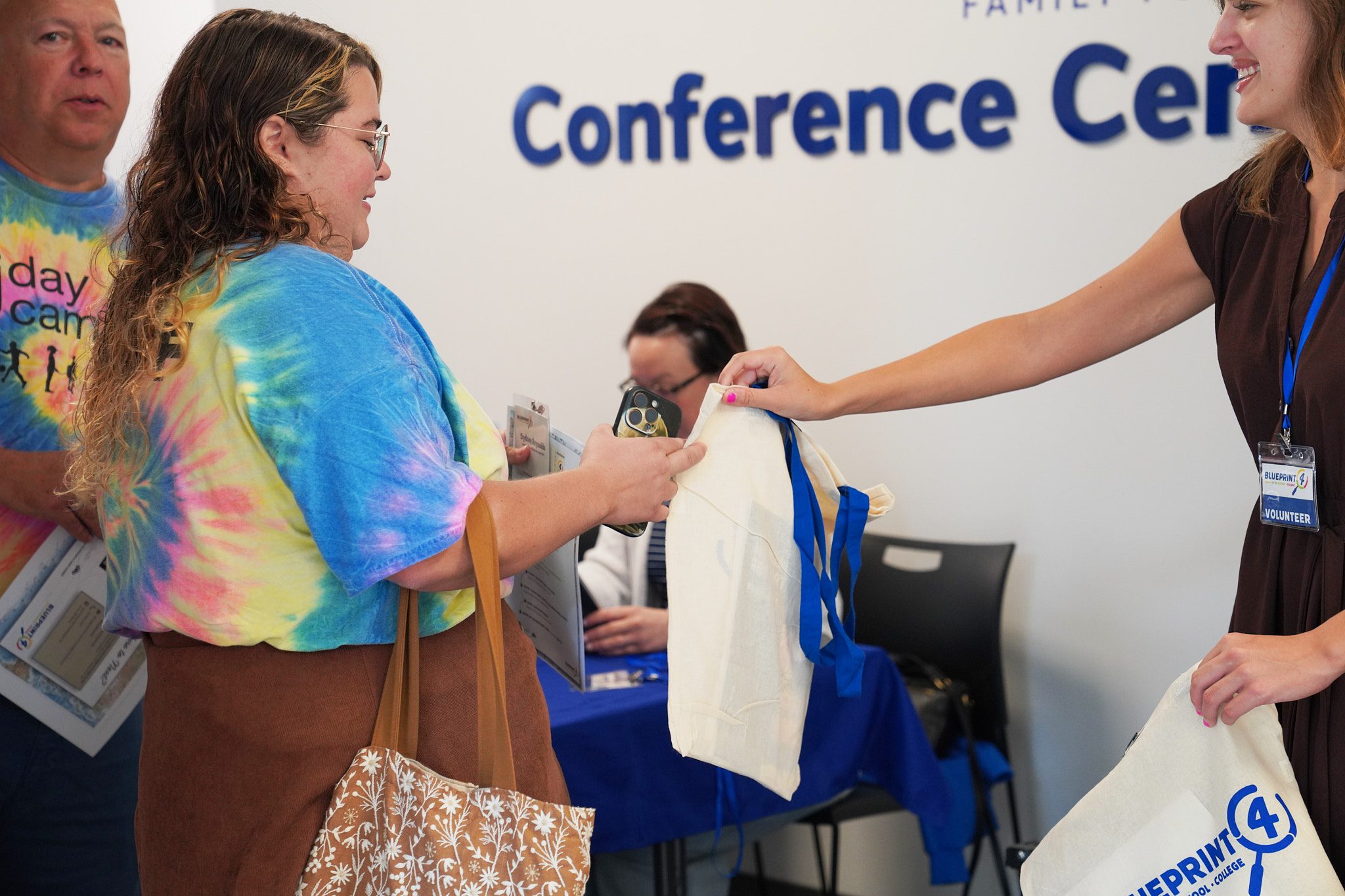 A woman checking in for the 2026 Camp Summit is handed a canvas bag printed with the Blueprint4 logo.