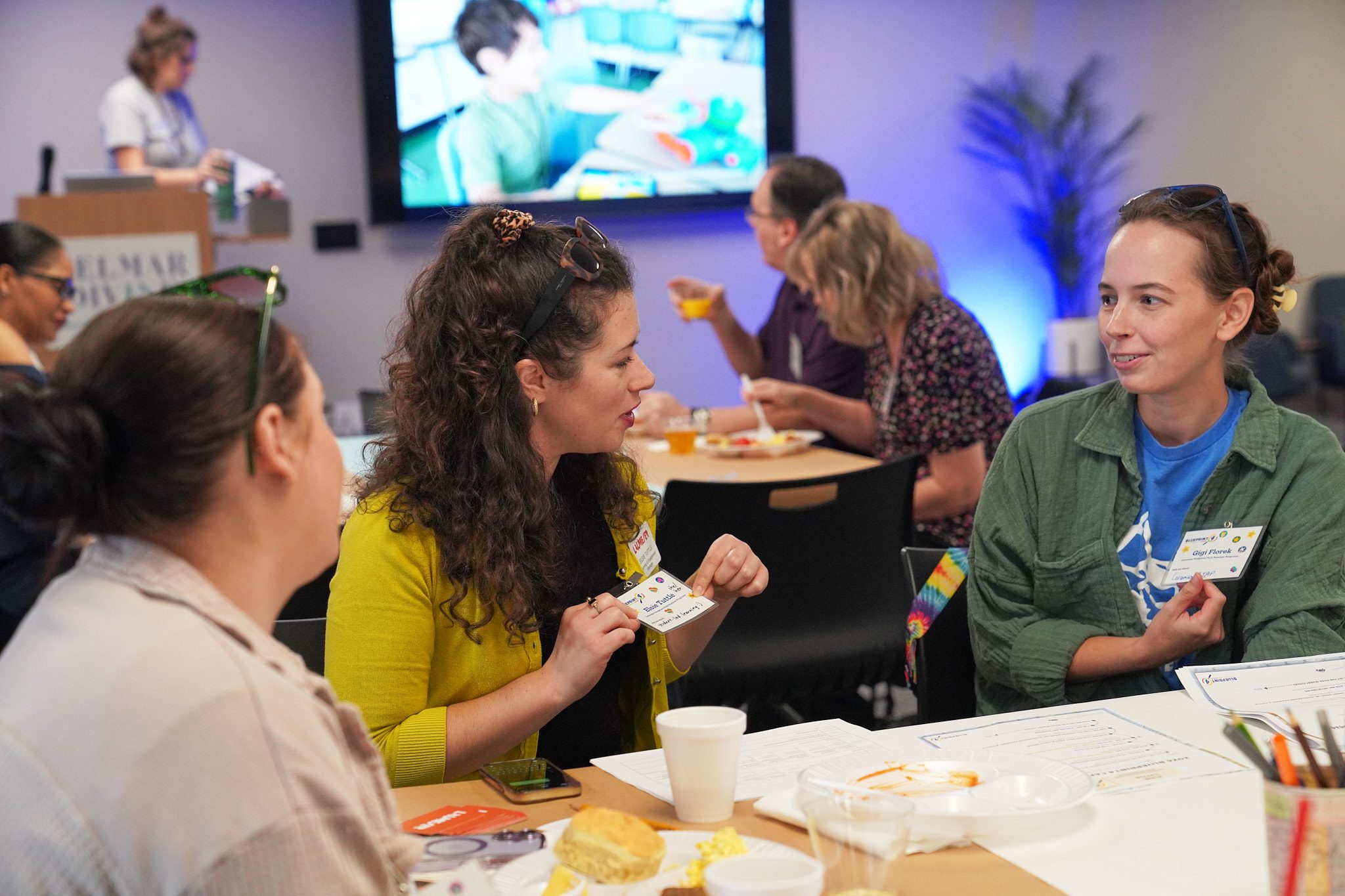 Camp providers sitting at a table together show their name tags to each other. The name tags have been decorated with stickers.