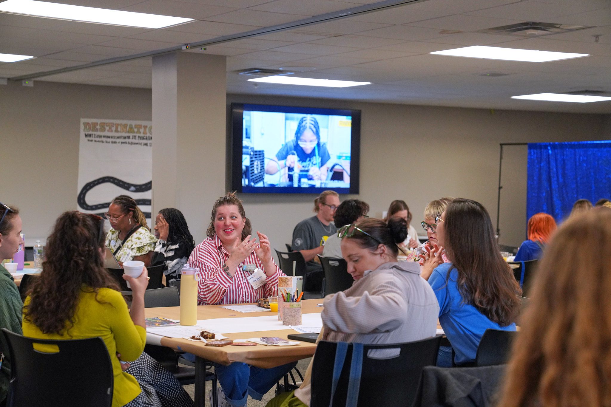 Camp providers chat among themselves at the 2026 Blueprint4 Camp Summit. One woman in a red and white striped shirt stands out as she gestures to another woman sitting across the table.