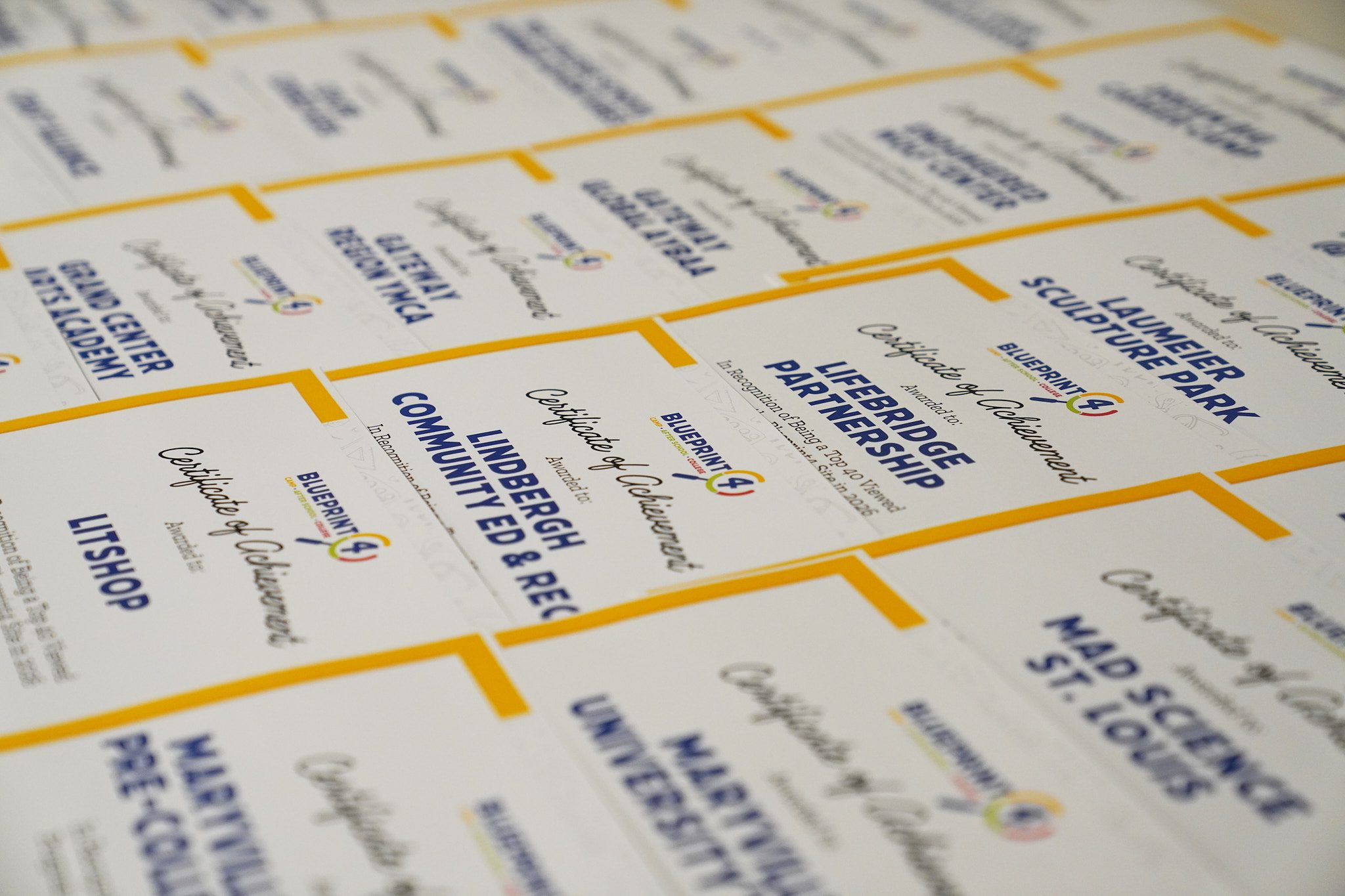 Certificates listing different St. Louis summer camps lie on a table waiting for camp providers to pick them up.