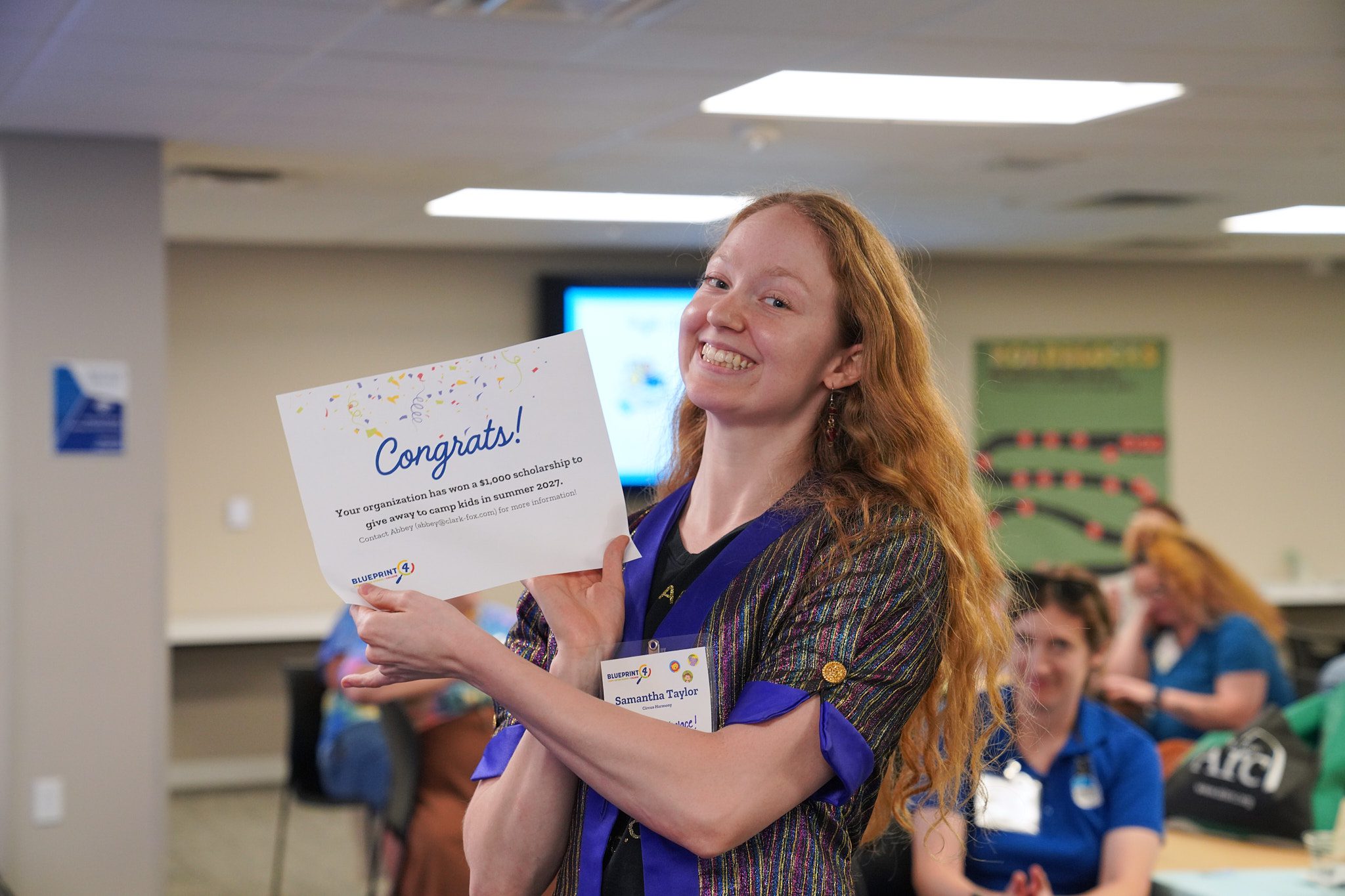 A woman from Circus Harmony holds up a certificate saying that her organization has won a $1,000 scholarship in a raffle.