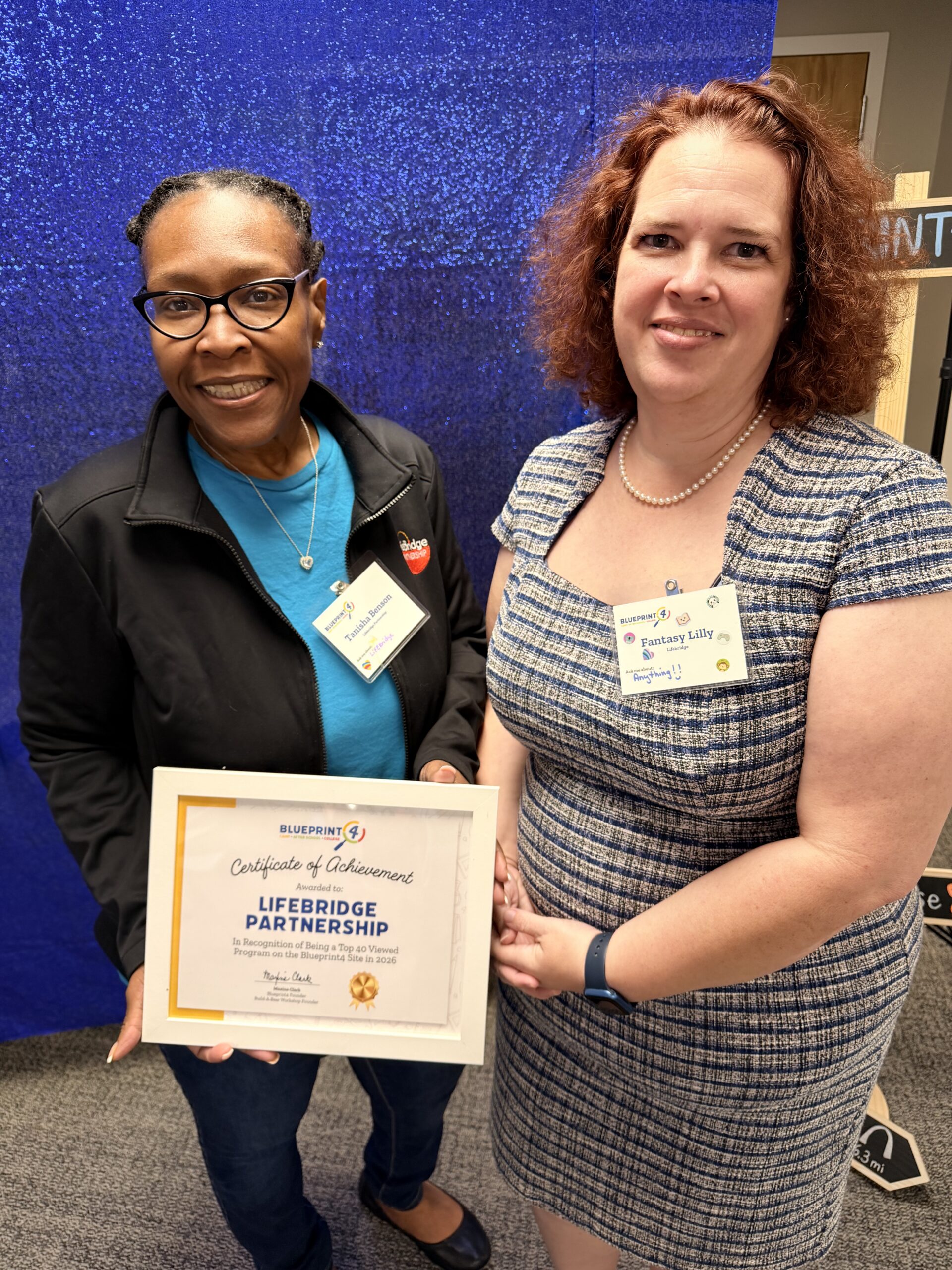 Camp providers from Lifebridge Partnership pose in front of a sparkly blue backdrop with their certificate of achievement.