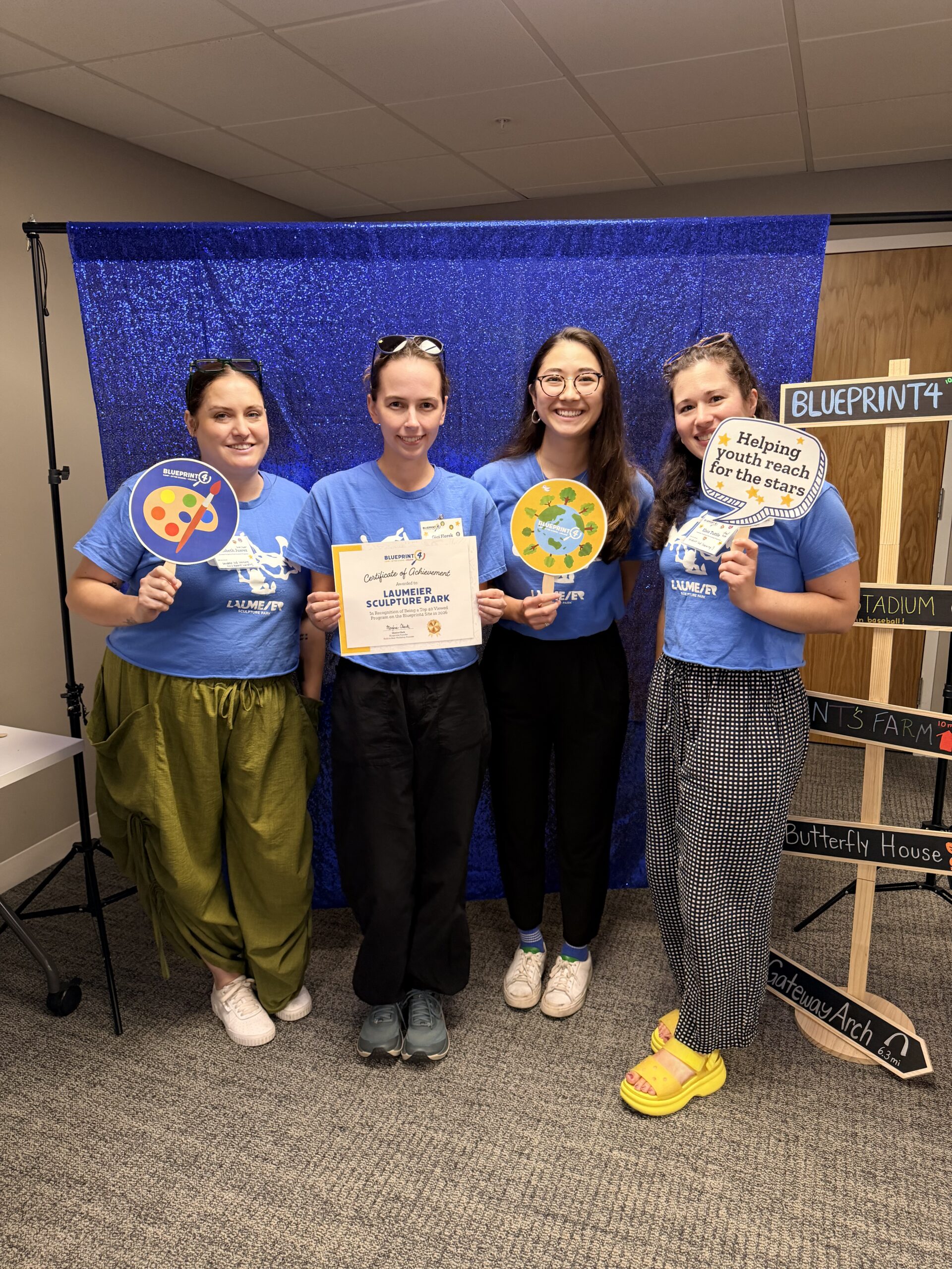 Camp providers from Laumeier Sculpture Park pose in front of a sparkly blue backdrop with their certificate of achievement.